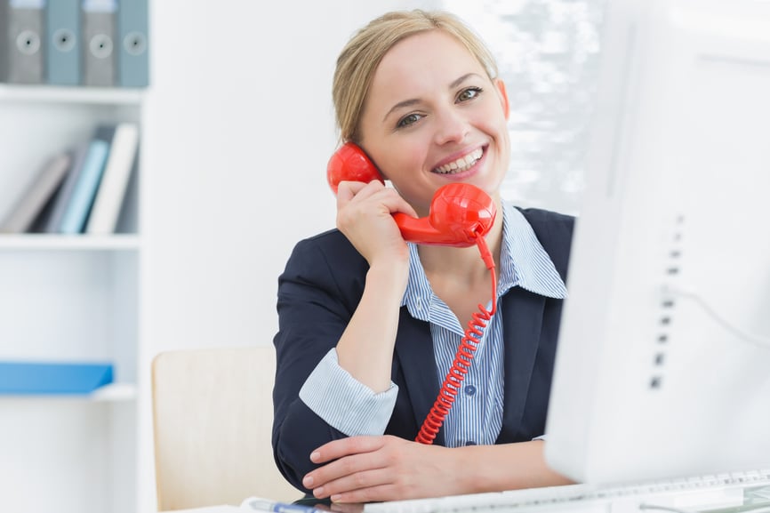 Portrait of smiling young female executive using red land line phone at desk in office
