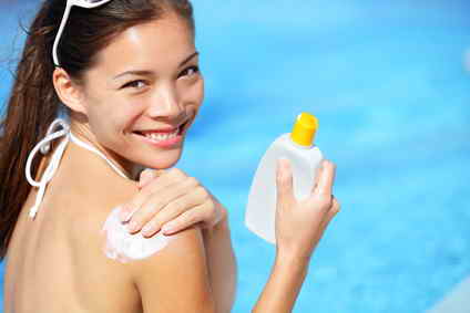 Smiling woman putting on sunscreen with pool in background