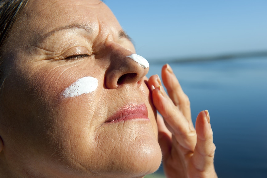 attractive mature woman with suncream on her face to protect herself from skin cancer, isolated with blurred background and copy space.