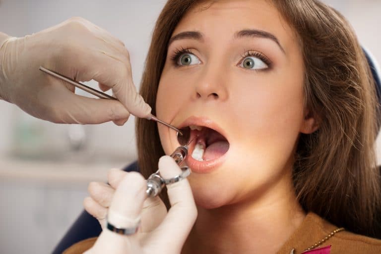 Dentist making anesthetic injection to scared female patient