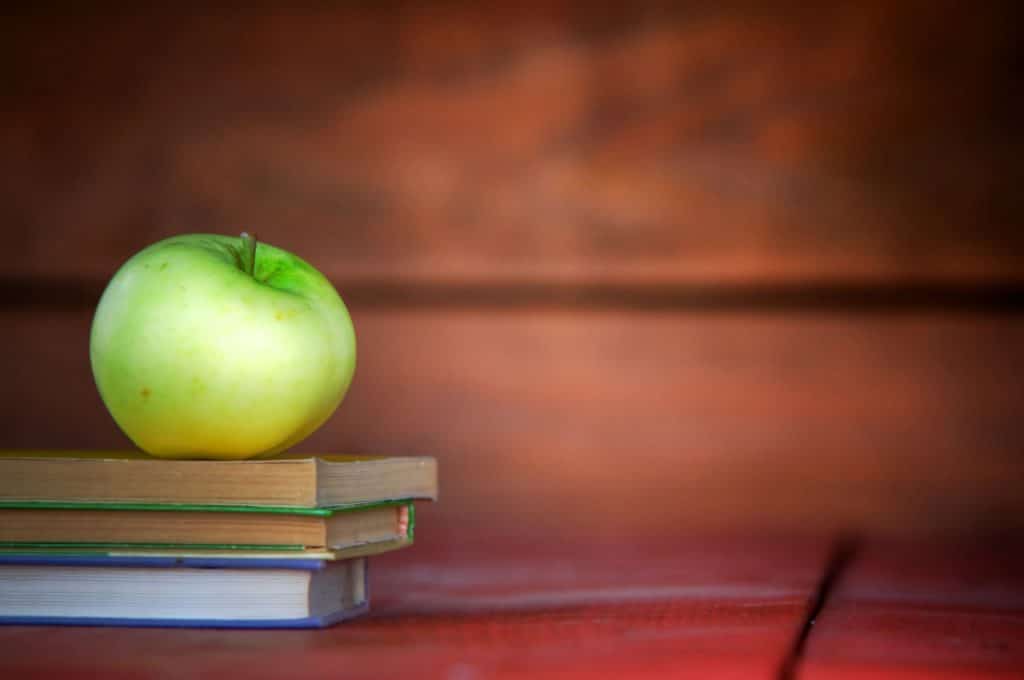 Green apple sitting on top of text books with redish background