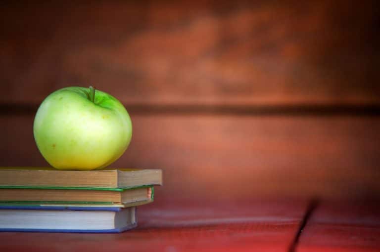 Green apple sitting on top of text books with redish background