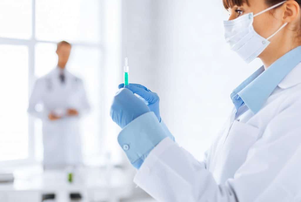 Nurse holding syringe with instructor blurred in background