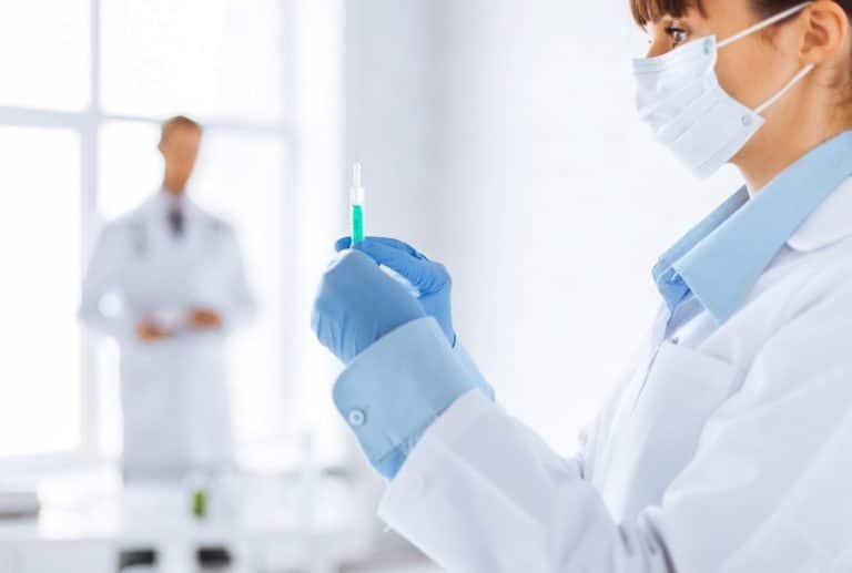 Nurse holding syringe with instructor blurred in background