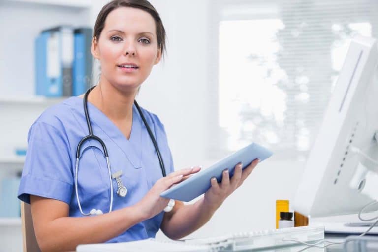 Nurse wearing stethoscope holding notebook looking at camera