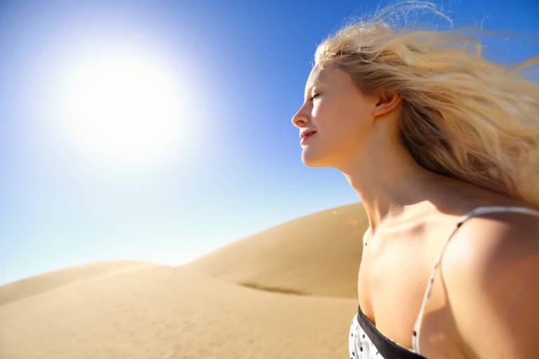 Blonde woman with eyes close and fair skin, hot wind blowing hair back, standing in desert with sun blazing down on her