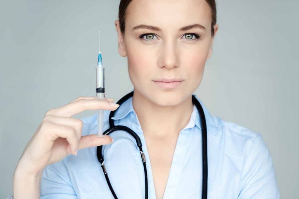 Nurse wearing stethoscope holding syringe looking into camera