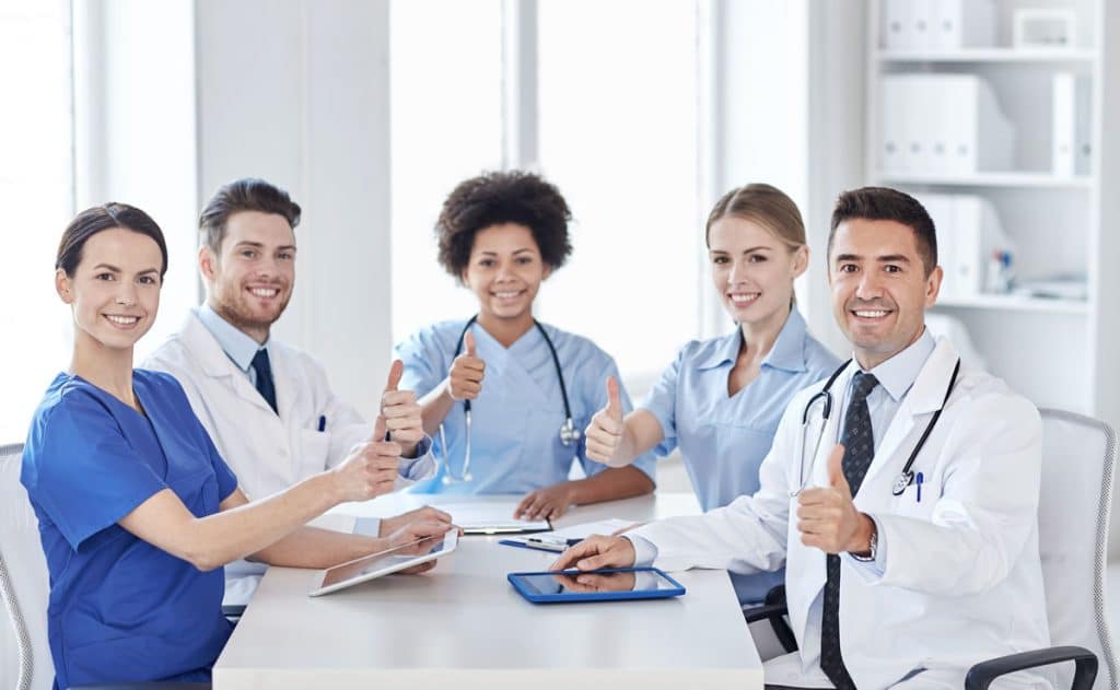 Several nurses and doctors sitting at table with laptops giving thumbs up