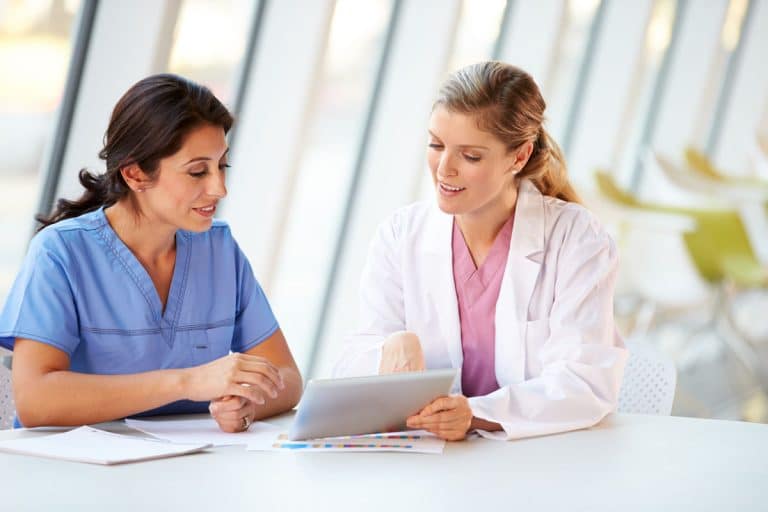 Doctor showing nurse information on laptop