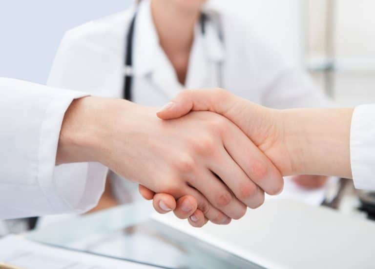 Two medical professional shaking hands with female medical professional blurred in background