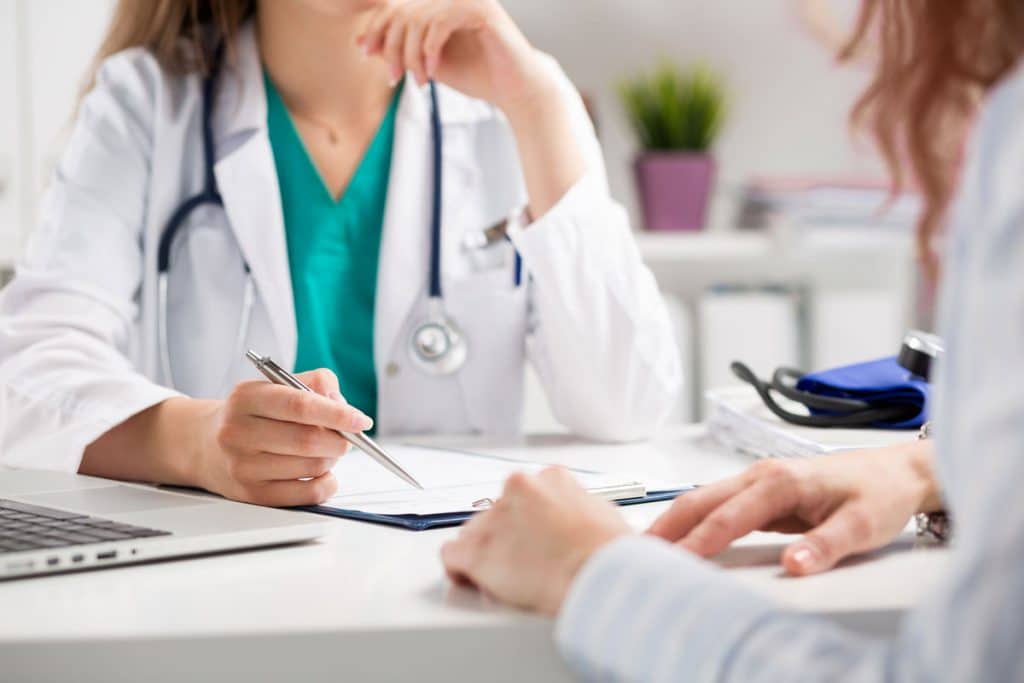 Below chin view of doctor with stethoscope, pen in hand talking with female student nurse