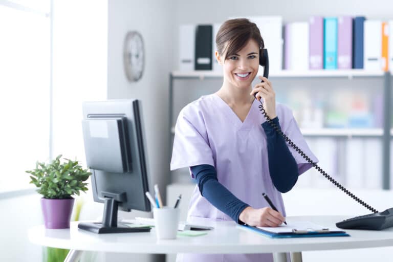 Woman answering phone wear purple long sleeved t-shirt under a lavender short sleeve scrub