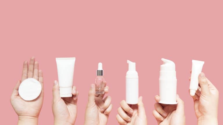 6 hands holding up different bottles and vials for applying, and containing skin care creams and liquids