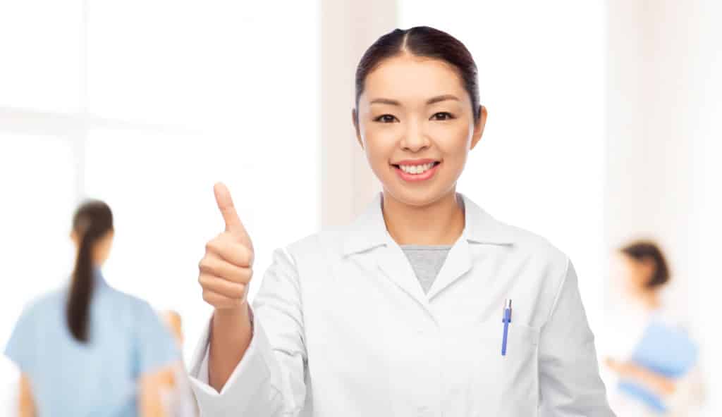 A nurse giving a thumbs up with fellow students blurred out behind her