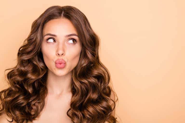 Young woman with dark curly hair looking up and making kiss mouth