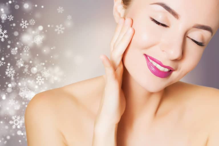 Smiling woman touching her face with animated snowflakes in background